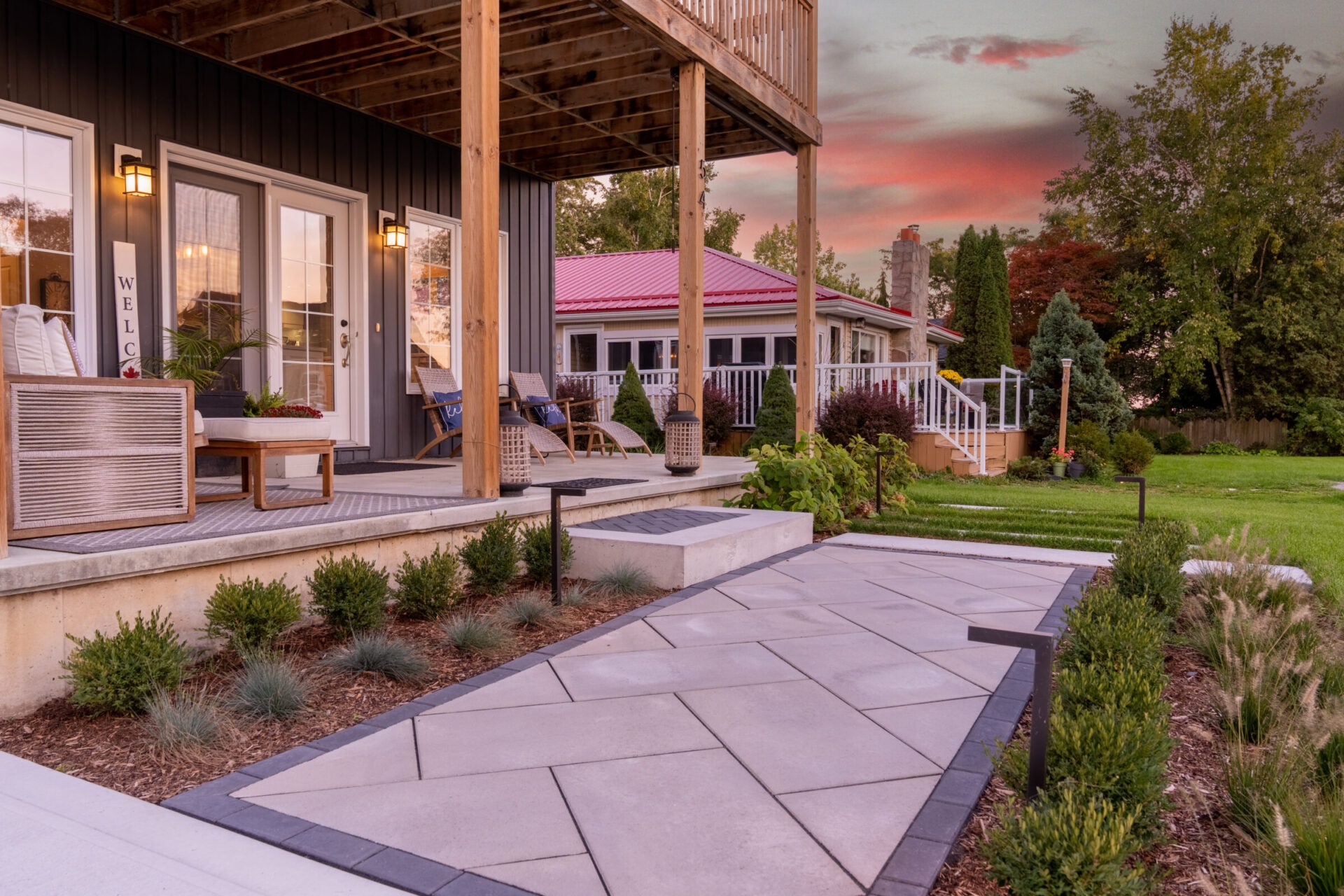 A serene backyard at dusk with well-manicured lawns, a modern patio area, comfortable outdoor furniture, landscaping, and a colorful sunset sky.