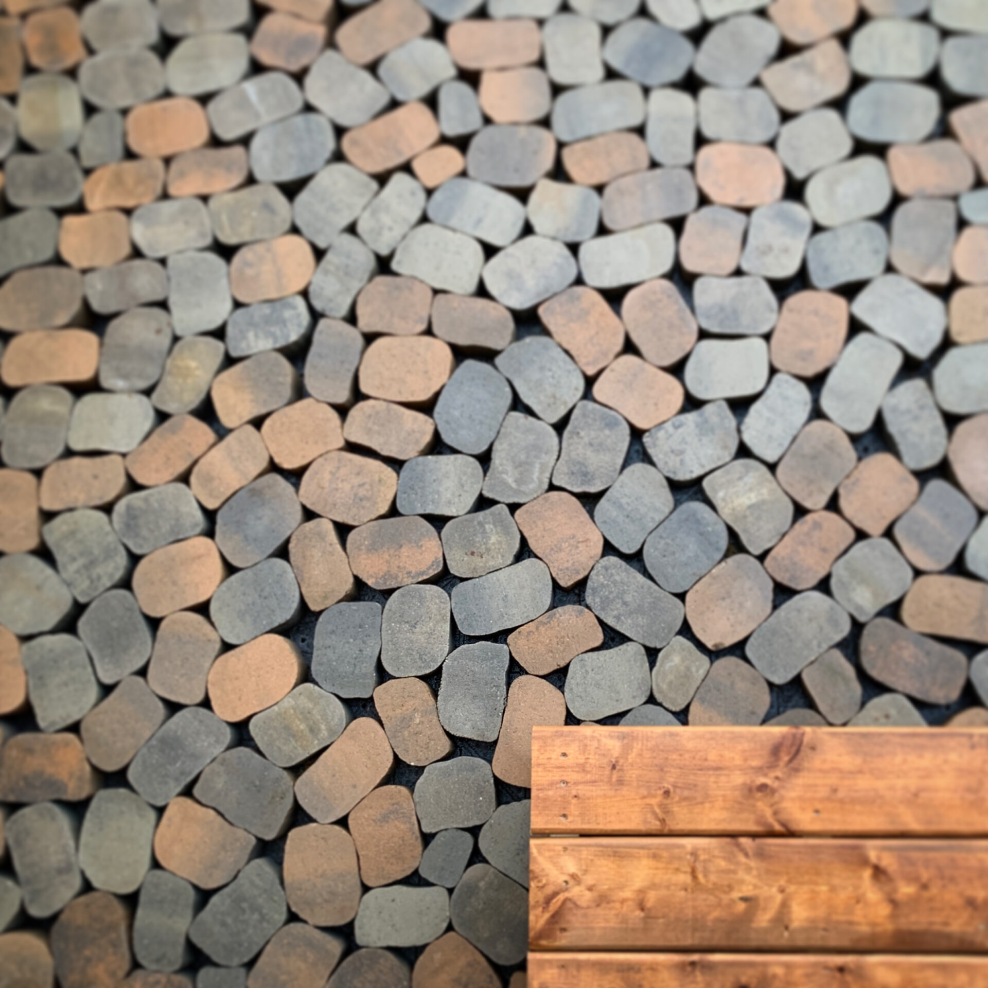 The image shows a cobblestone surface transitioning into a wooden floor, with varied stone hues and textures next to smooth wood planks.