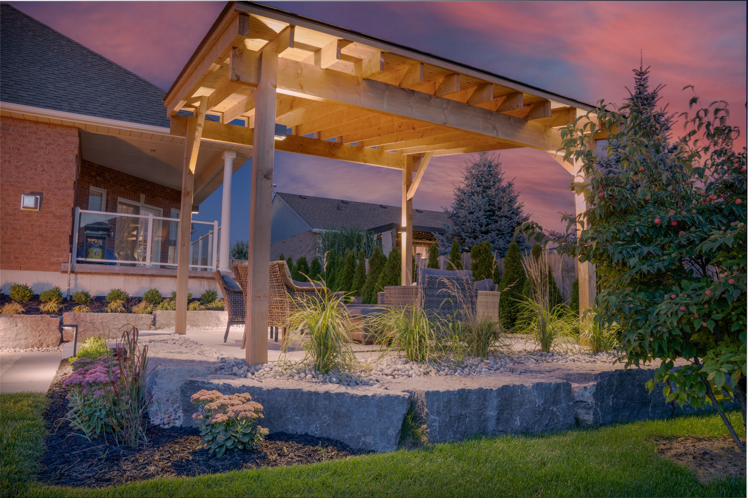 A serene backyard at dusk features a pergola, stylish garden beds, outdoor furniture, and a well-kept lawn against a colorful evening sky.