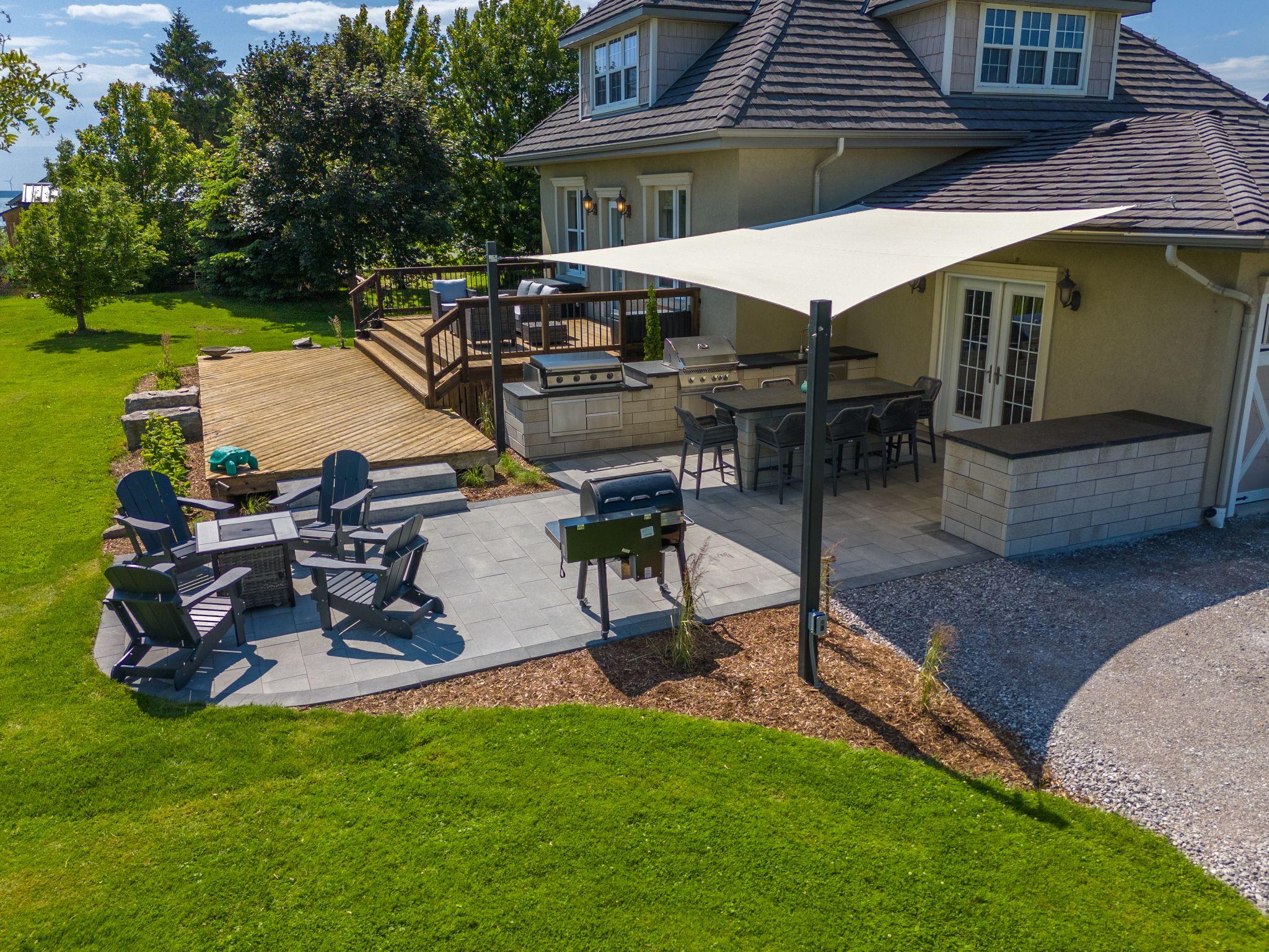 Backyard outdoor kitchen and patio with shade sail, grilling area, and green lawn