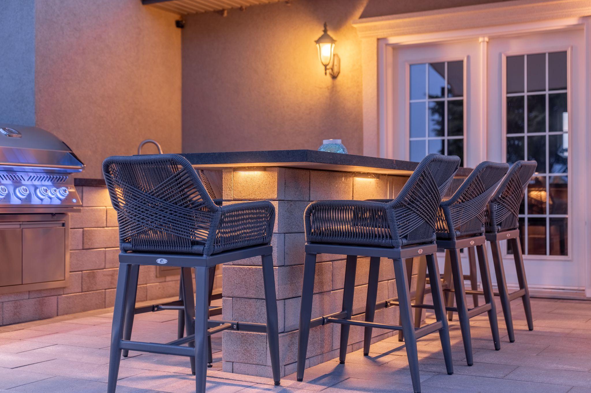 Modern outdoor bar with built-in grill and seating under warm lighting