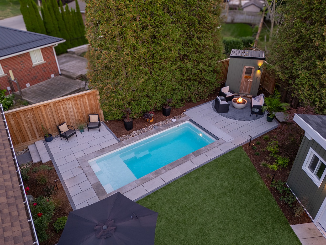 Aerial view of a clean, modern rectangular pool with light grey stone coping, a matching stone patio, and an outdoor sauna, representing a low-maintenance and durable backyard spa retreat.