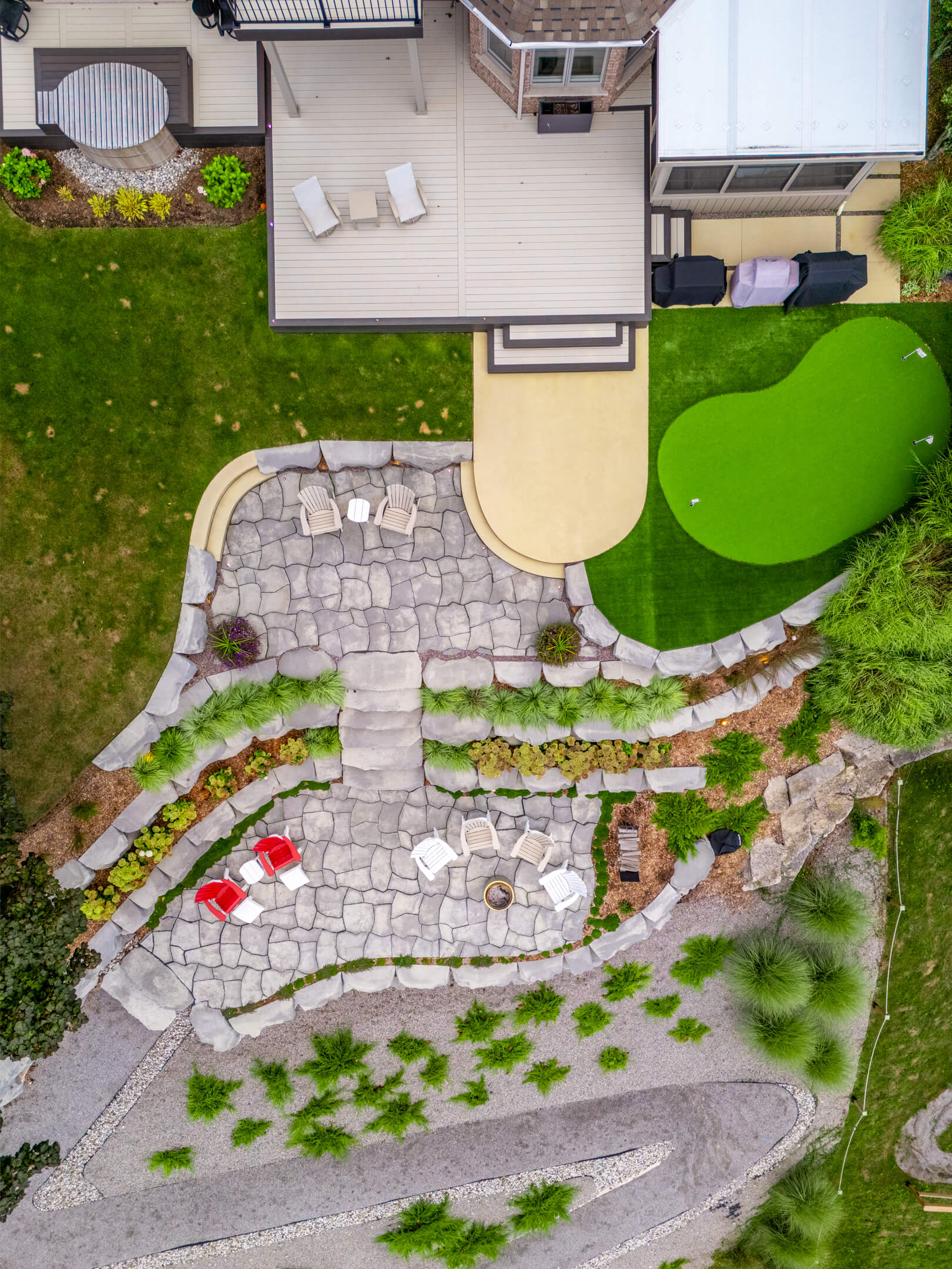 Directly overhead bird's-eye view of a tiered flagstone patio, putting green, and backyard landscaping.