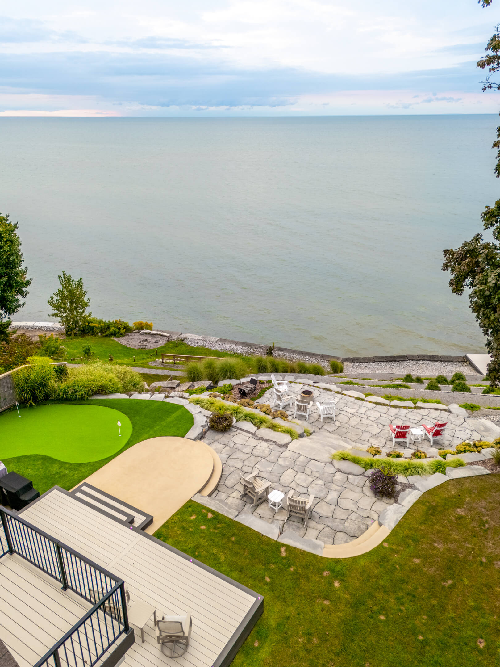 Aerial view of a stone patio with Adirondack chairs and a putting green overlooking a vast, blue lake.