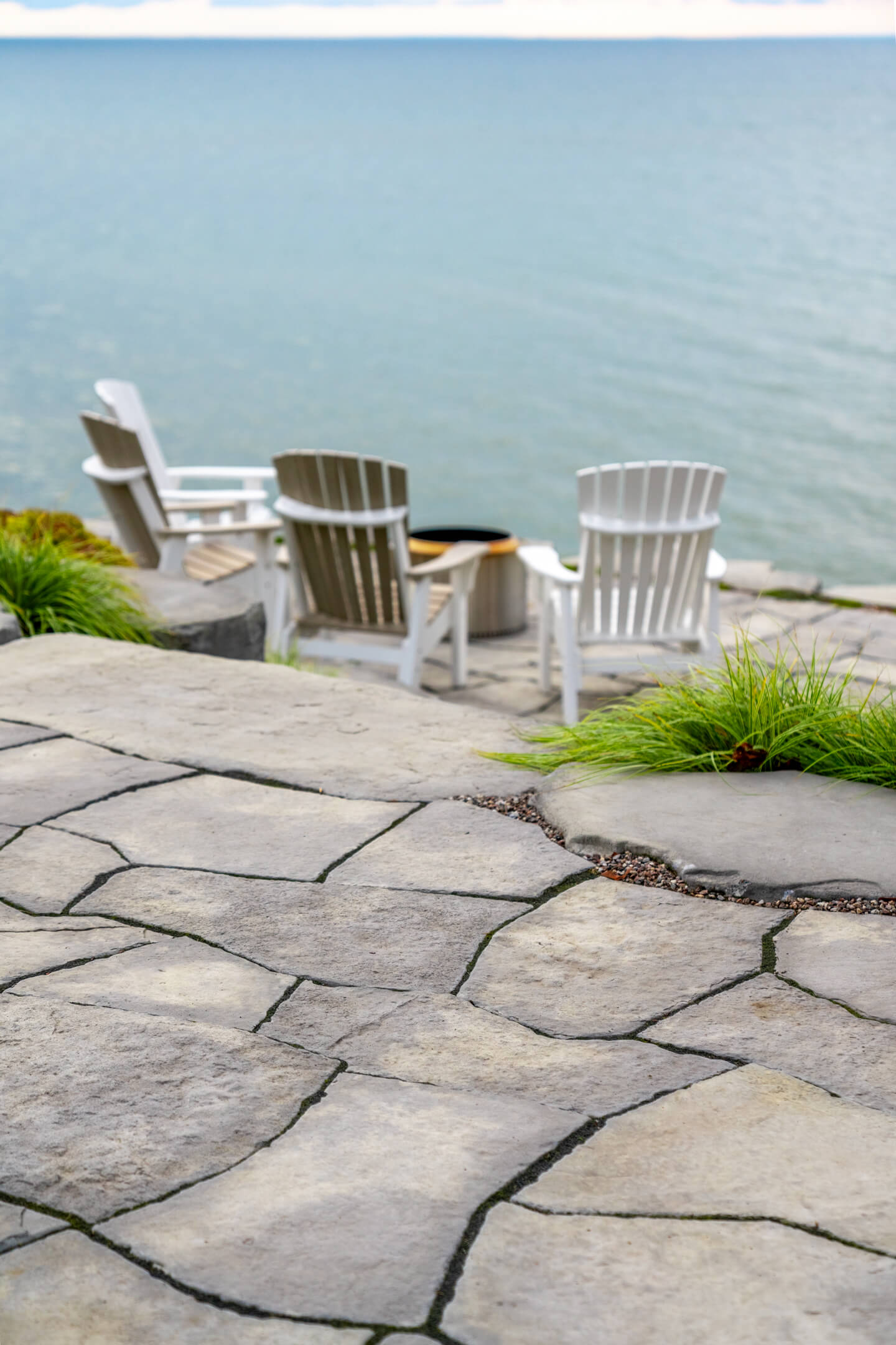High-angle view of an irregular flagstone patio with Adirondack chairs and a fire pit by the lake.
