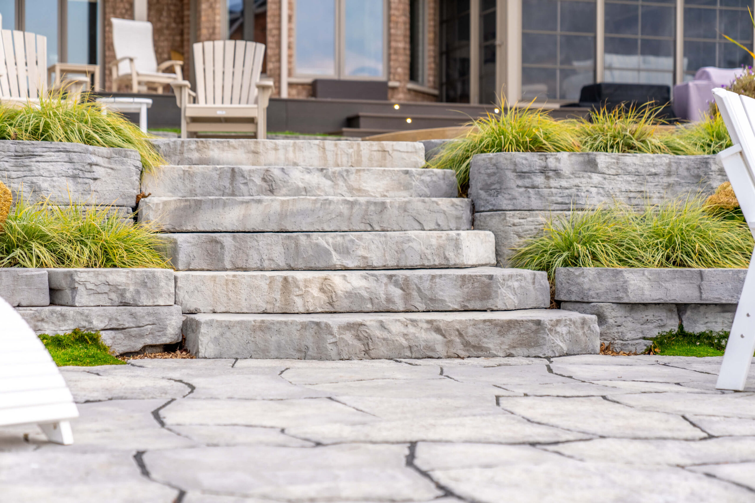 Low-angle view of massive textured stone stairs leading up to a lakeside patio and brick home.