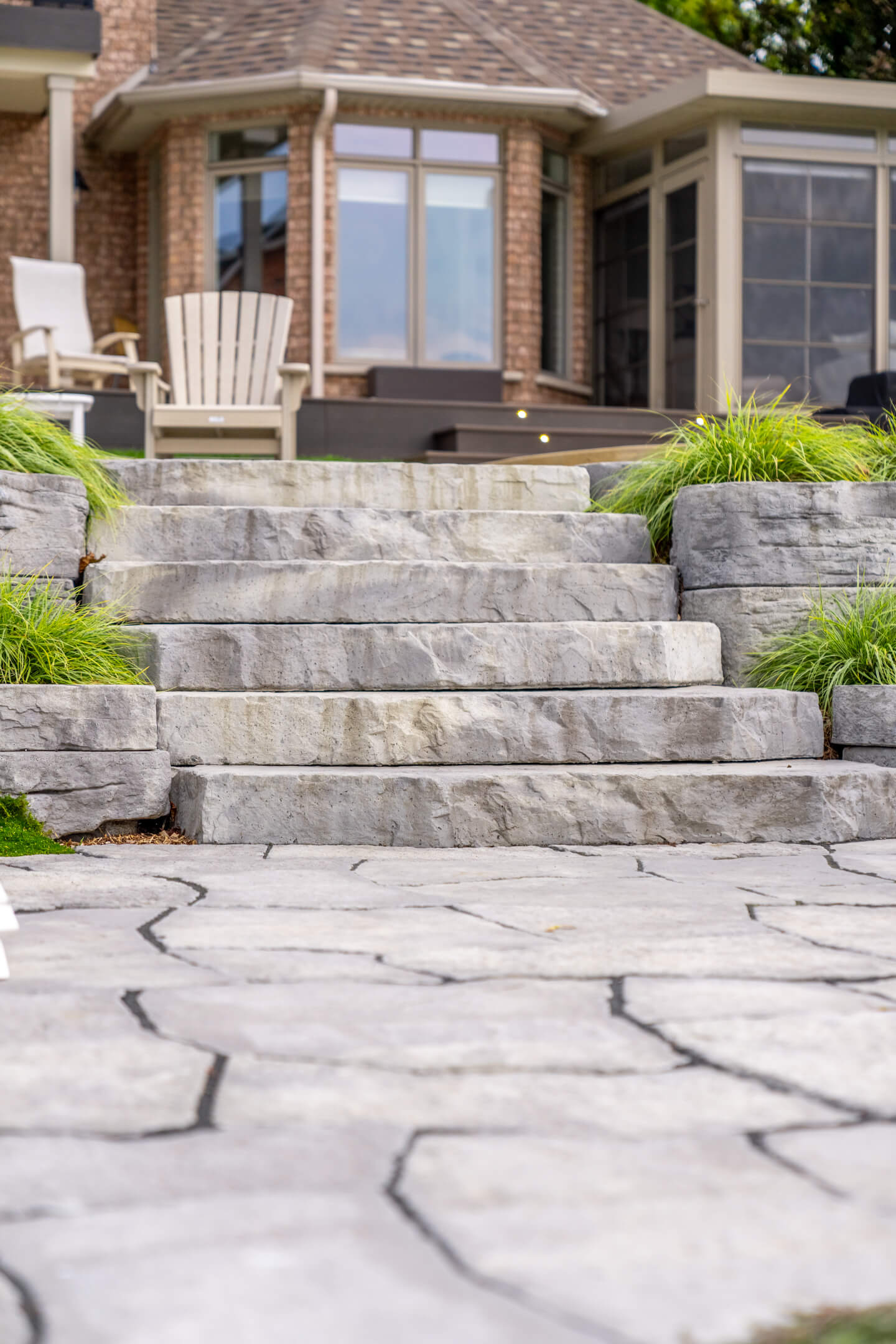 Wide stone steps integrated into a sloped landscape leading toward a large brick house with a sunroom.