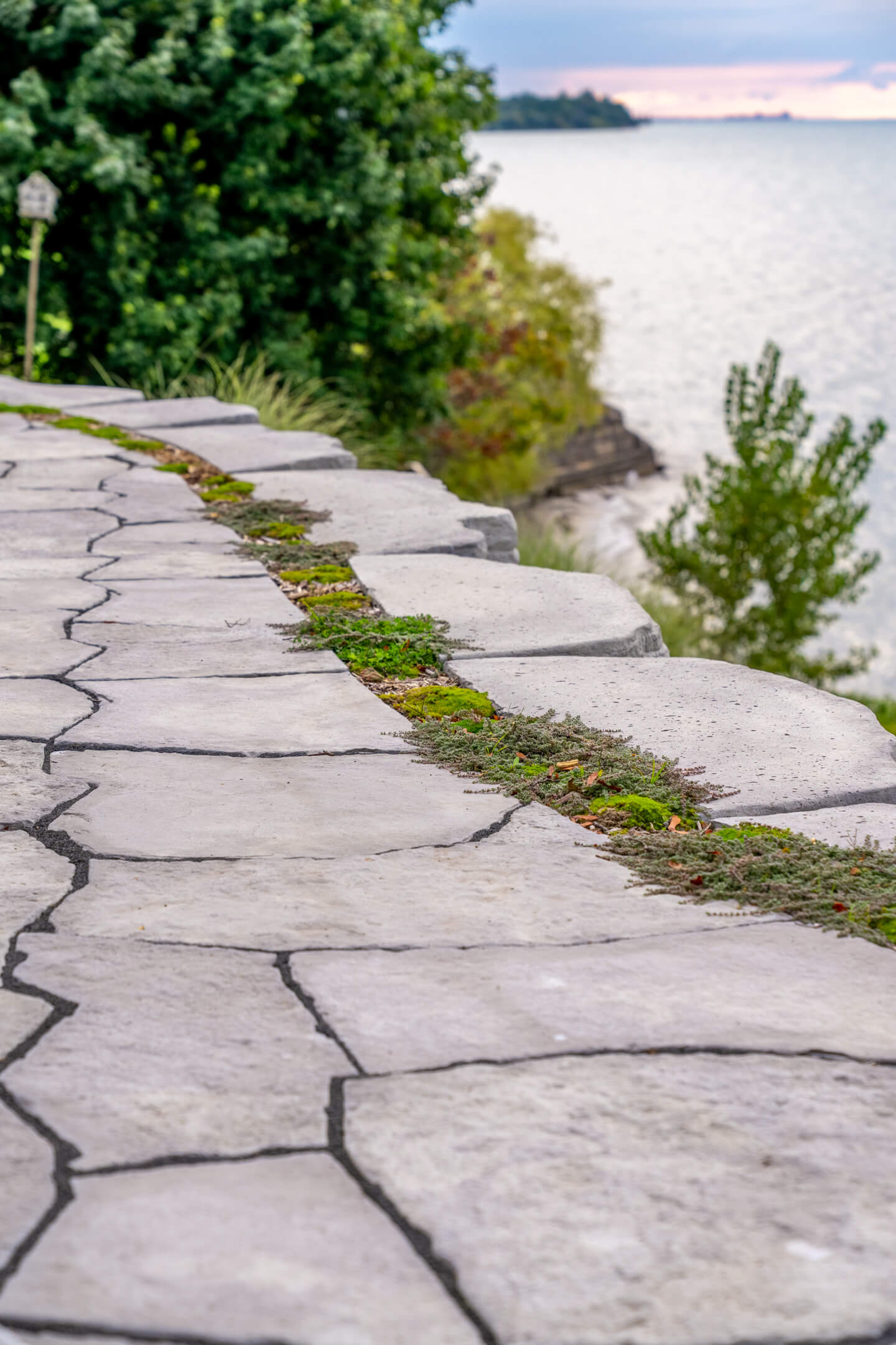 Perspective of a flagstone walkway along a cliffside overlooking a large lake at dusk.