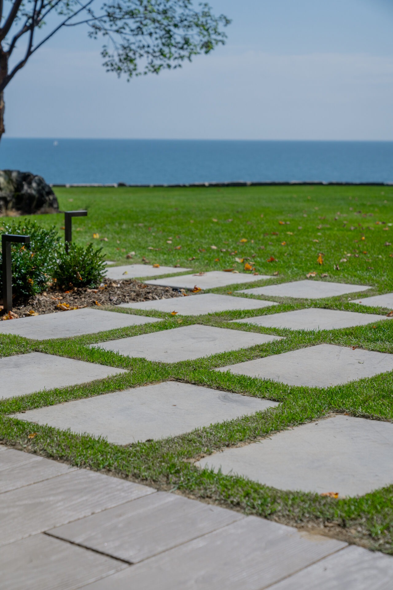 Square stone pavers set in a grid within a lush green lawn leading toward the blue lake.