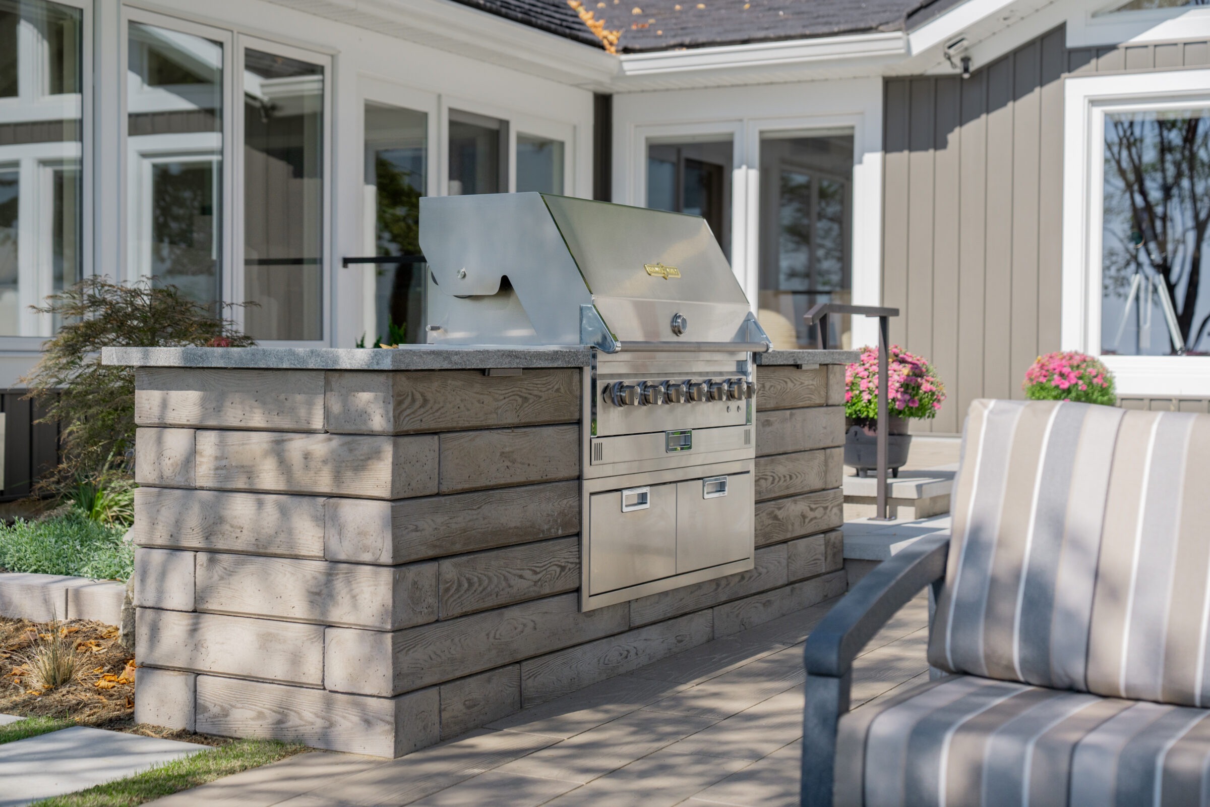 A high-end outdoor kitchen island with a stainless steel grill and stone-textured siding.