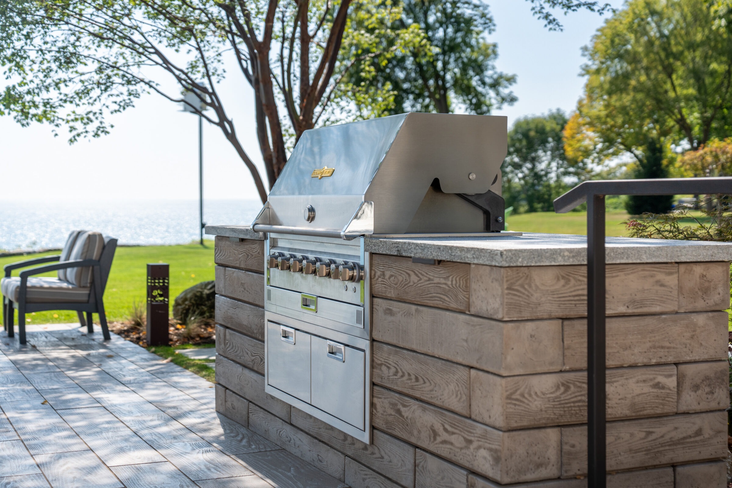 : Side view of an outdoor grill station overlooking a large blue lake on a sunny day.