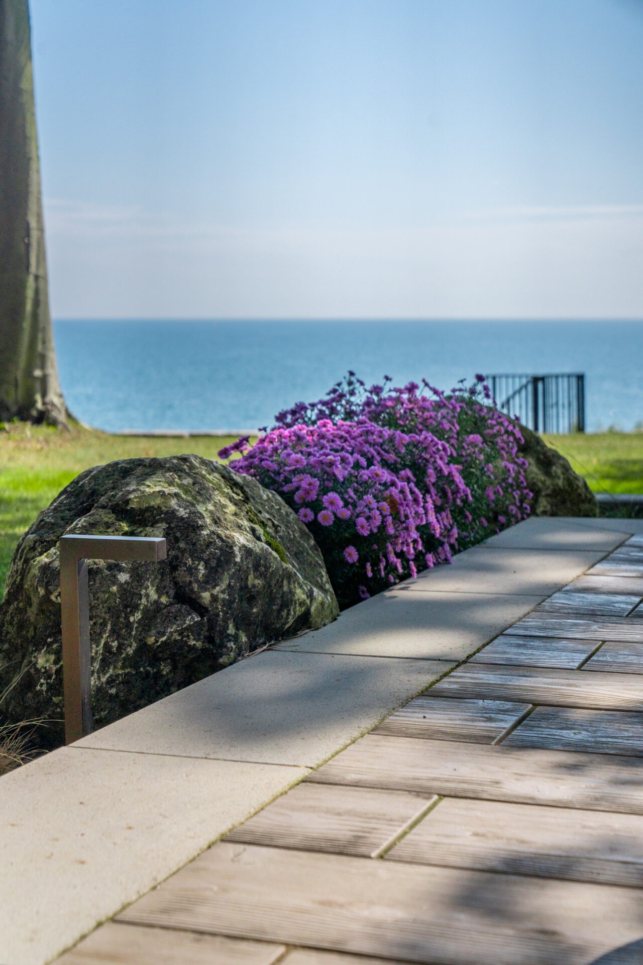 Vibrant purple flowers in a stone garden bed next to a patio, with a clear blue lake in the background.
