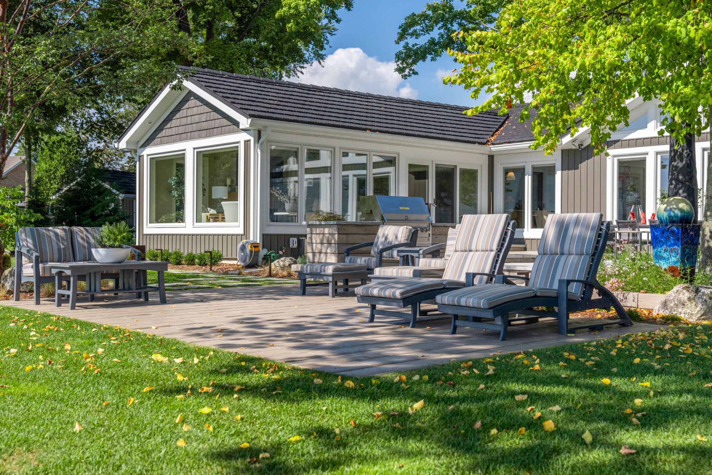 An outdoor lounge area with striped reclining chairs on a stone patio next to a modern home