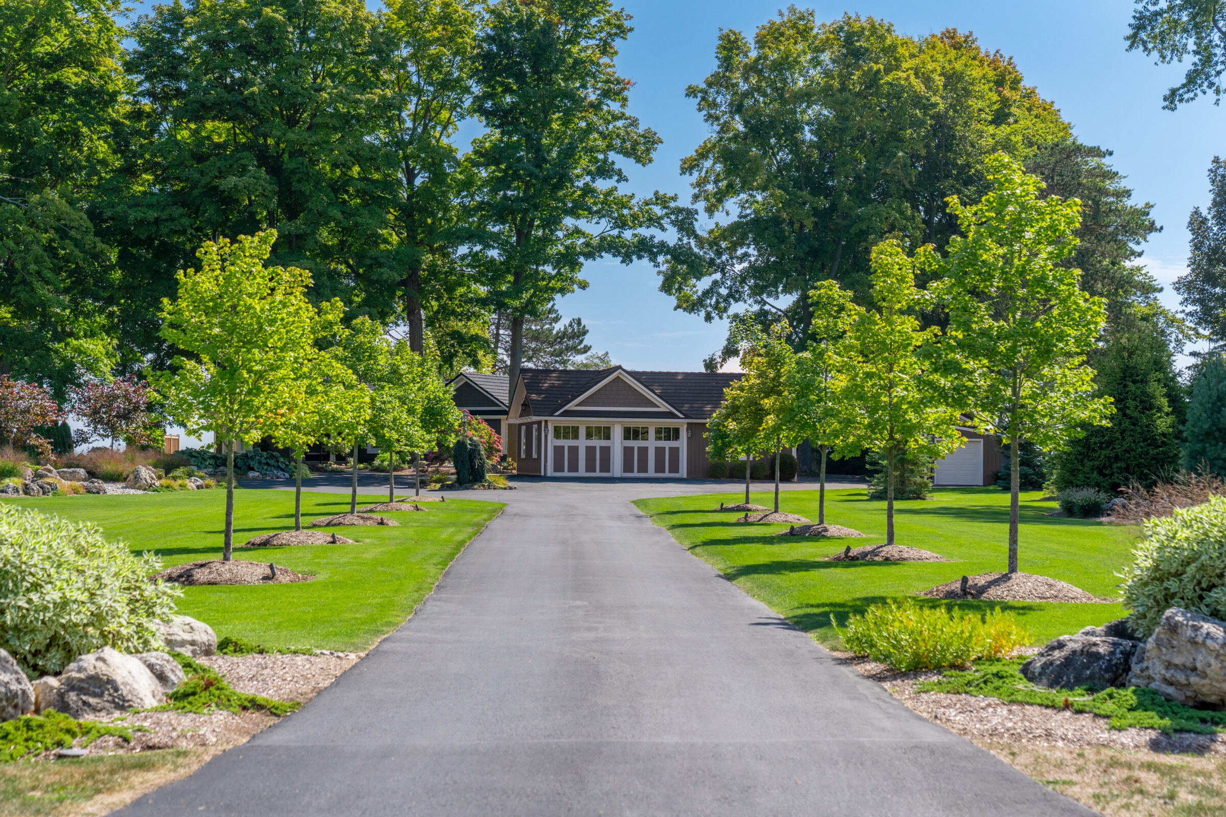 Wide view of a long driveway leading to a modern home with a large white garage and professional landscaping.