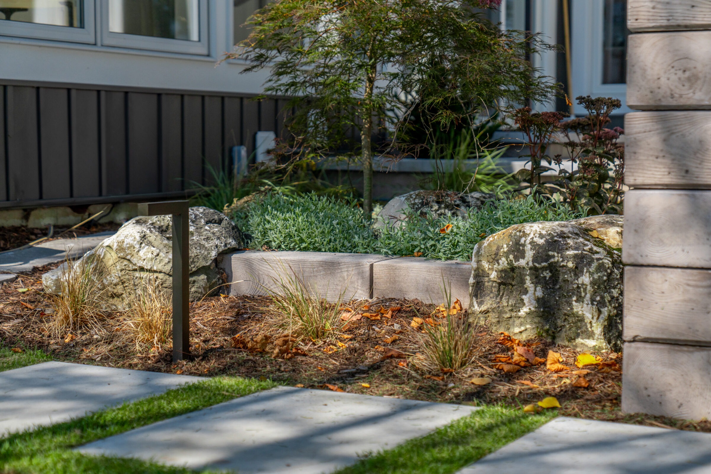 Close-up of a stone garden wall and landscaping with small shrubs, rocks, and a black light fixture.