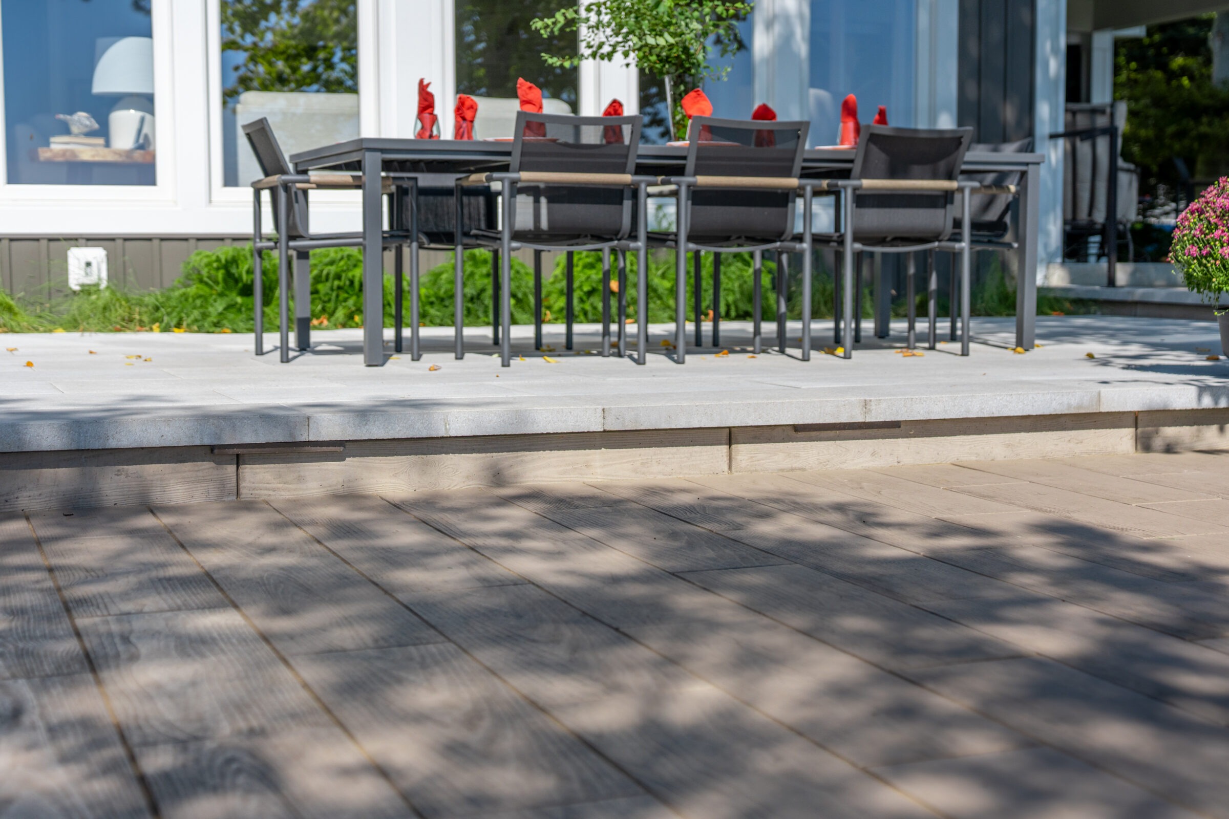 View of a modern patio dining set with red napkins, set on a clean stone terrace next to a house.