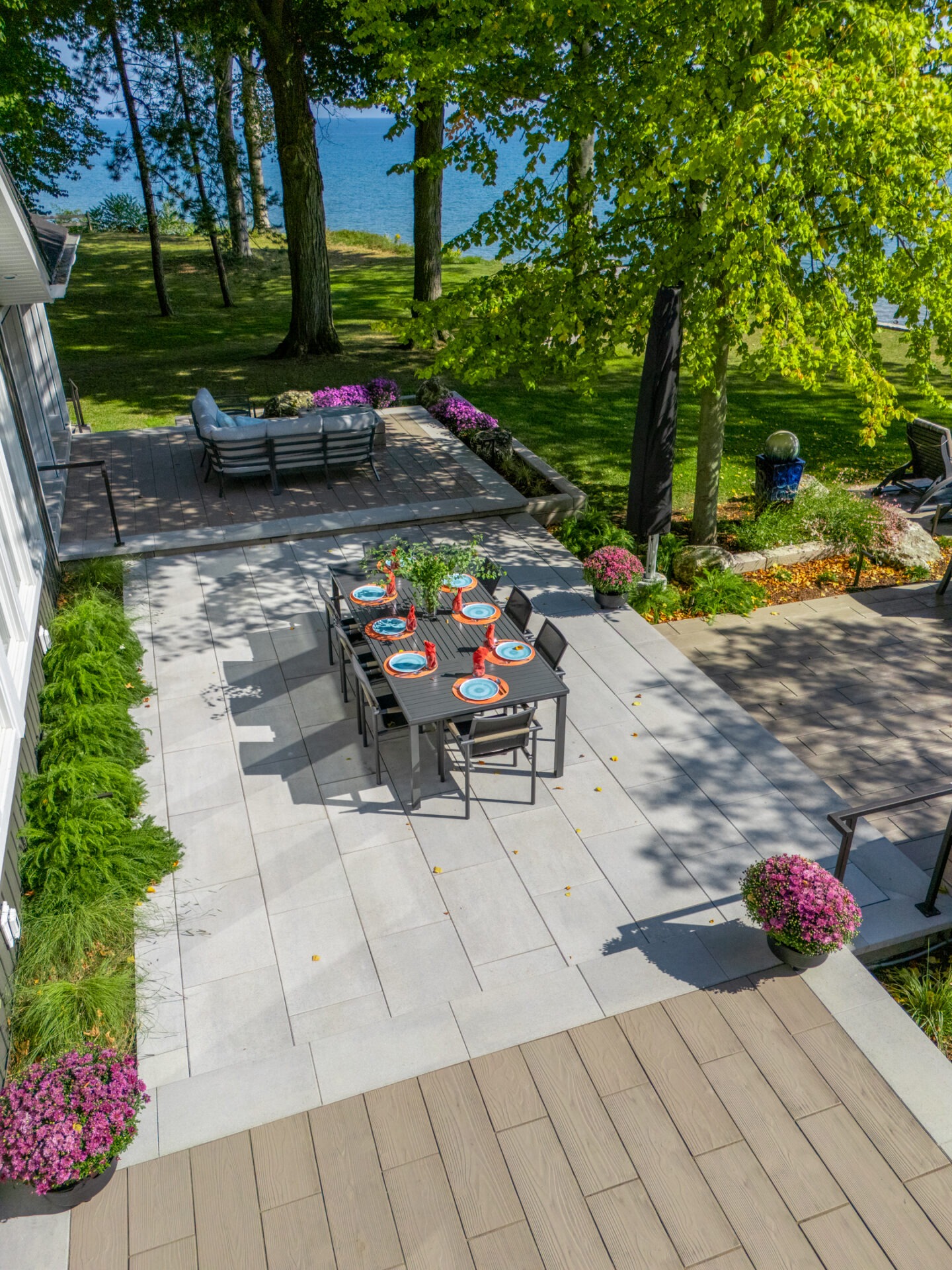 Aerial view of an outdoor dining table set for eight on a modern grey stone patio by the lake.