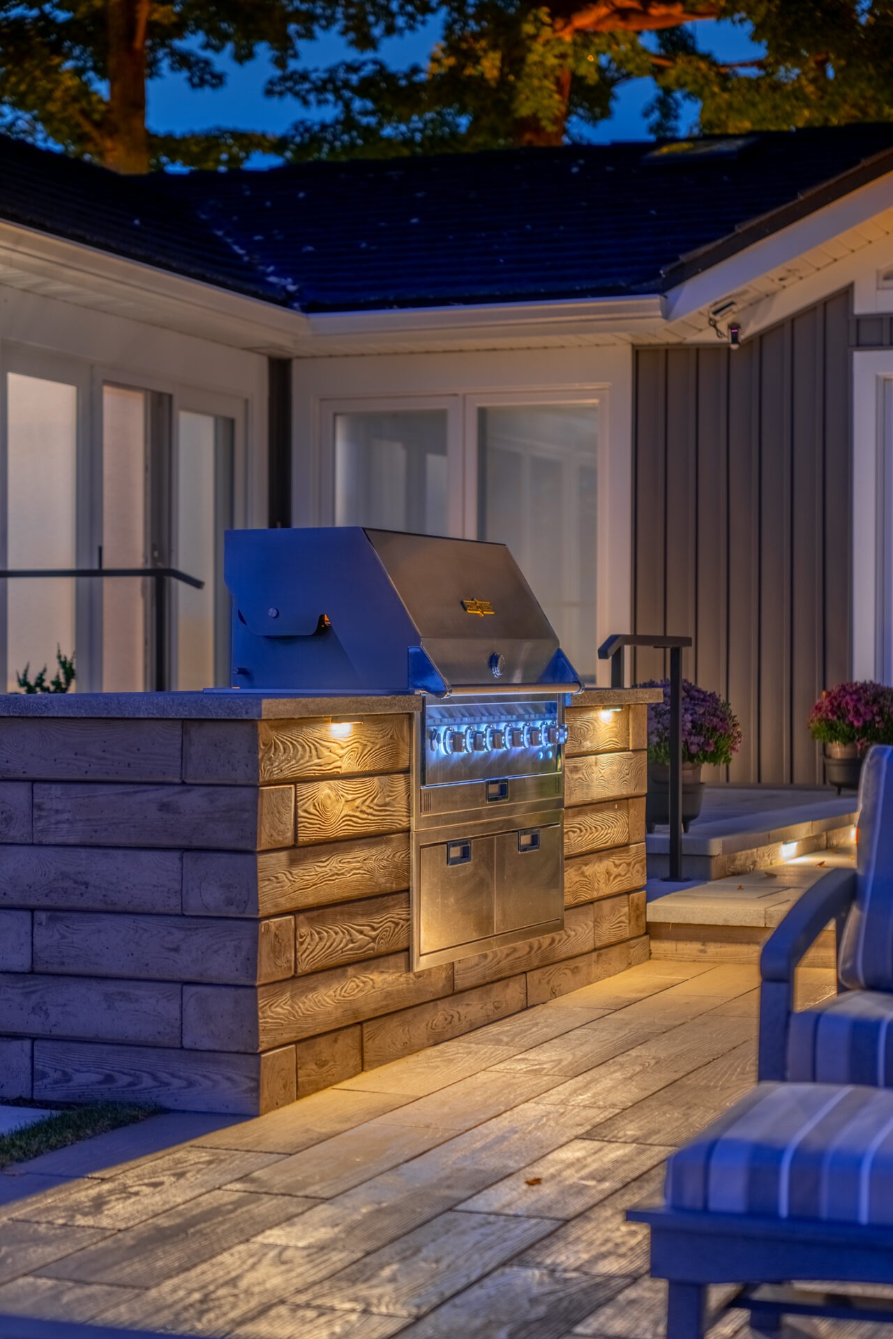 Evening shot of a built-in outdoor grill station illuminated by warm, integrated landscape lighting.