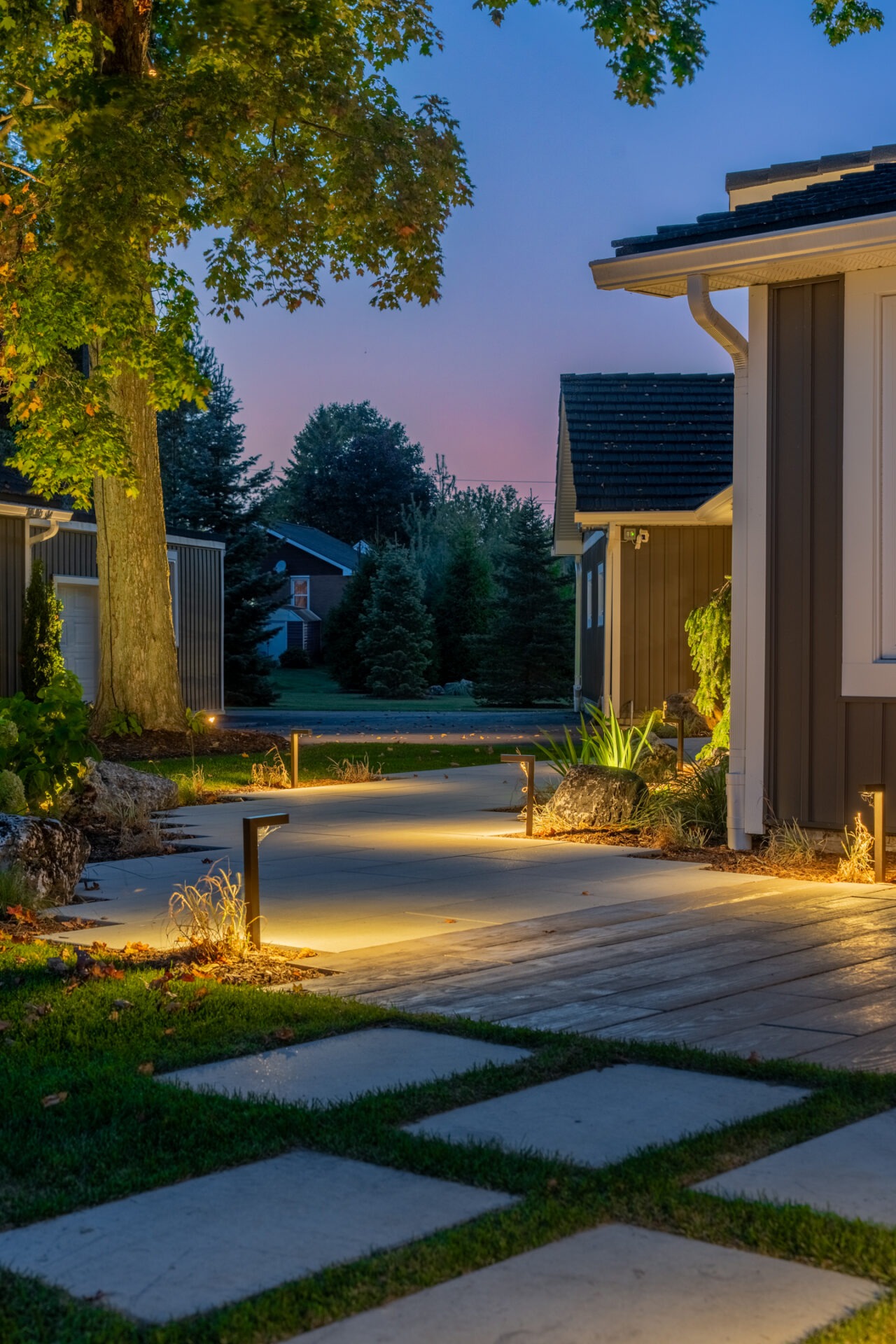 A scenic garden bed featuring large white boulders, dark-leafed trees, and tall ornamental grasses.