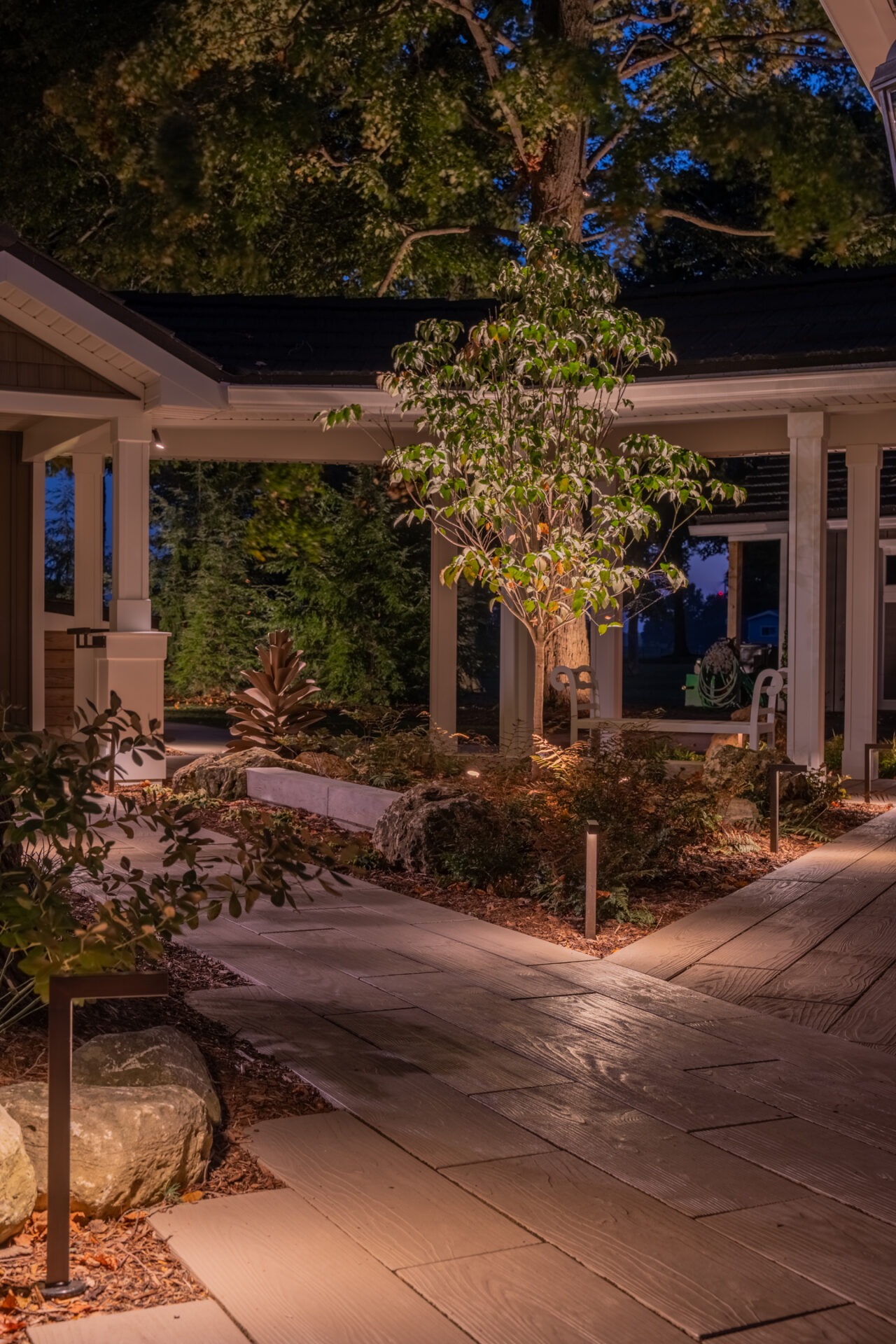 Night view of a garden courtyard with a lit tree, stone paths, and warm, integrated landscape lighting.