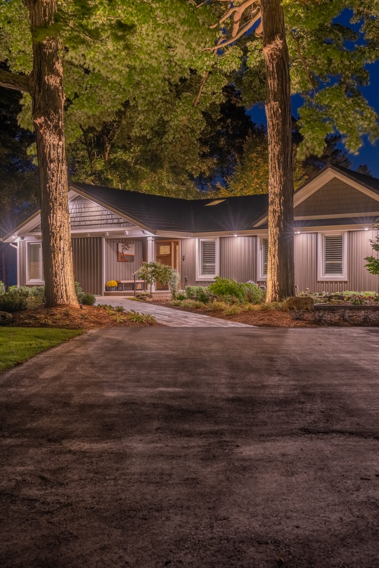 Night shot of a modern home exterior featuring grey siding and warm lighting reflecting off an asphalt driveway.