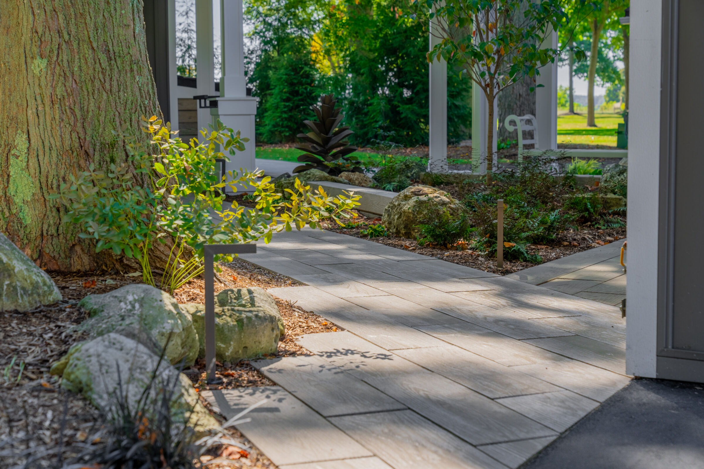 A stone path winding through a garden with large rocks, landscape lighting, and mature trees.
