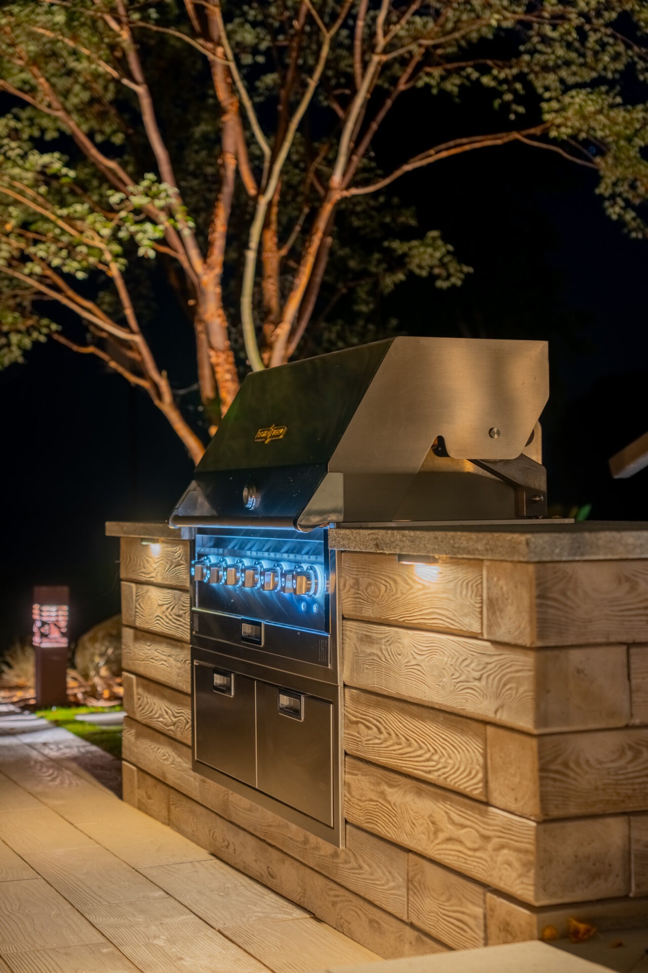 Close-up of a high-end outdoor grill station with integrated blue and warm white lighting at night.