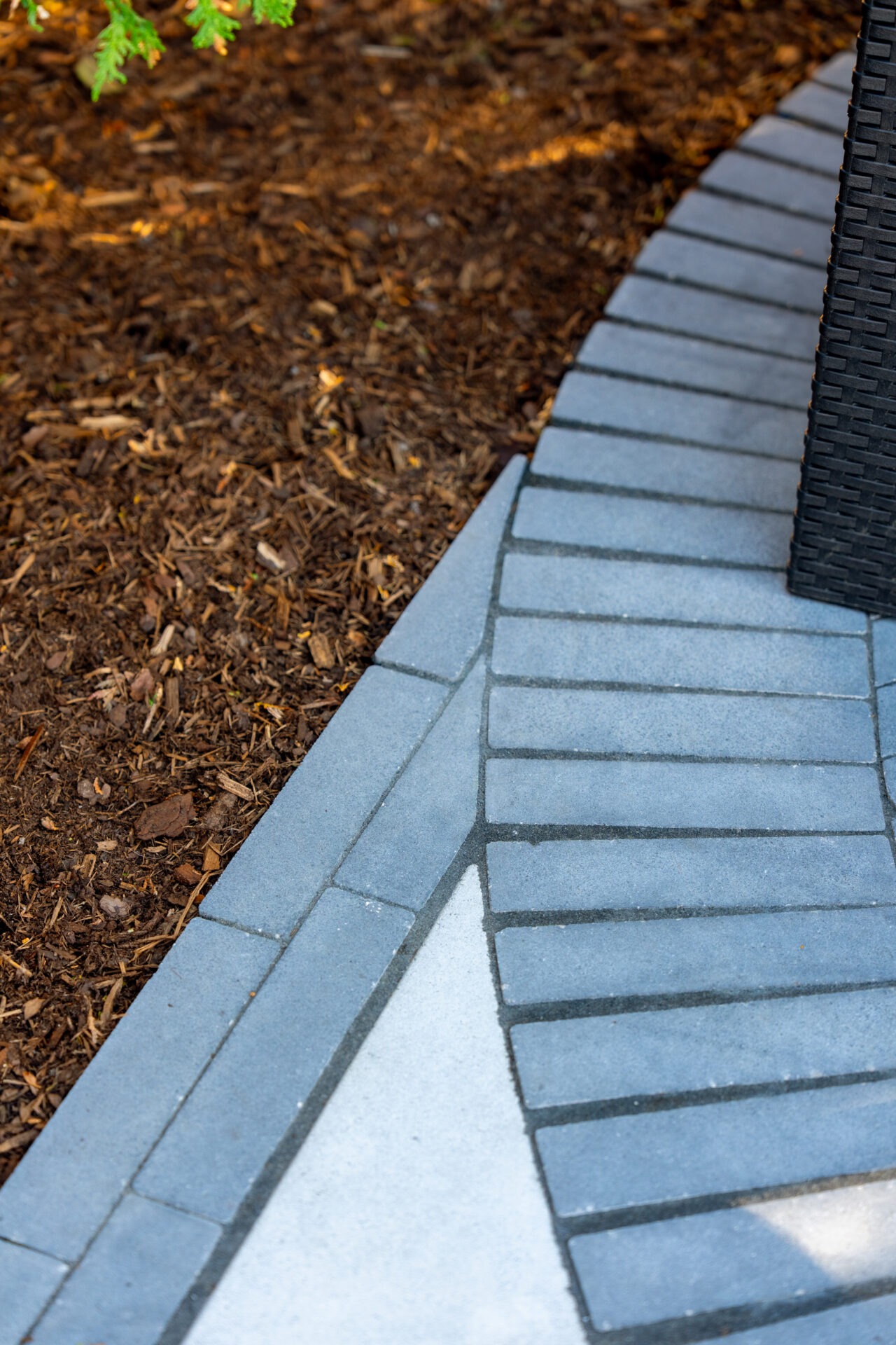 Detail of dark grey rectangular pavers meeting a light stone border and brown wood mulch in a garden bed.