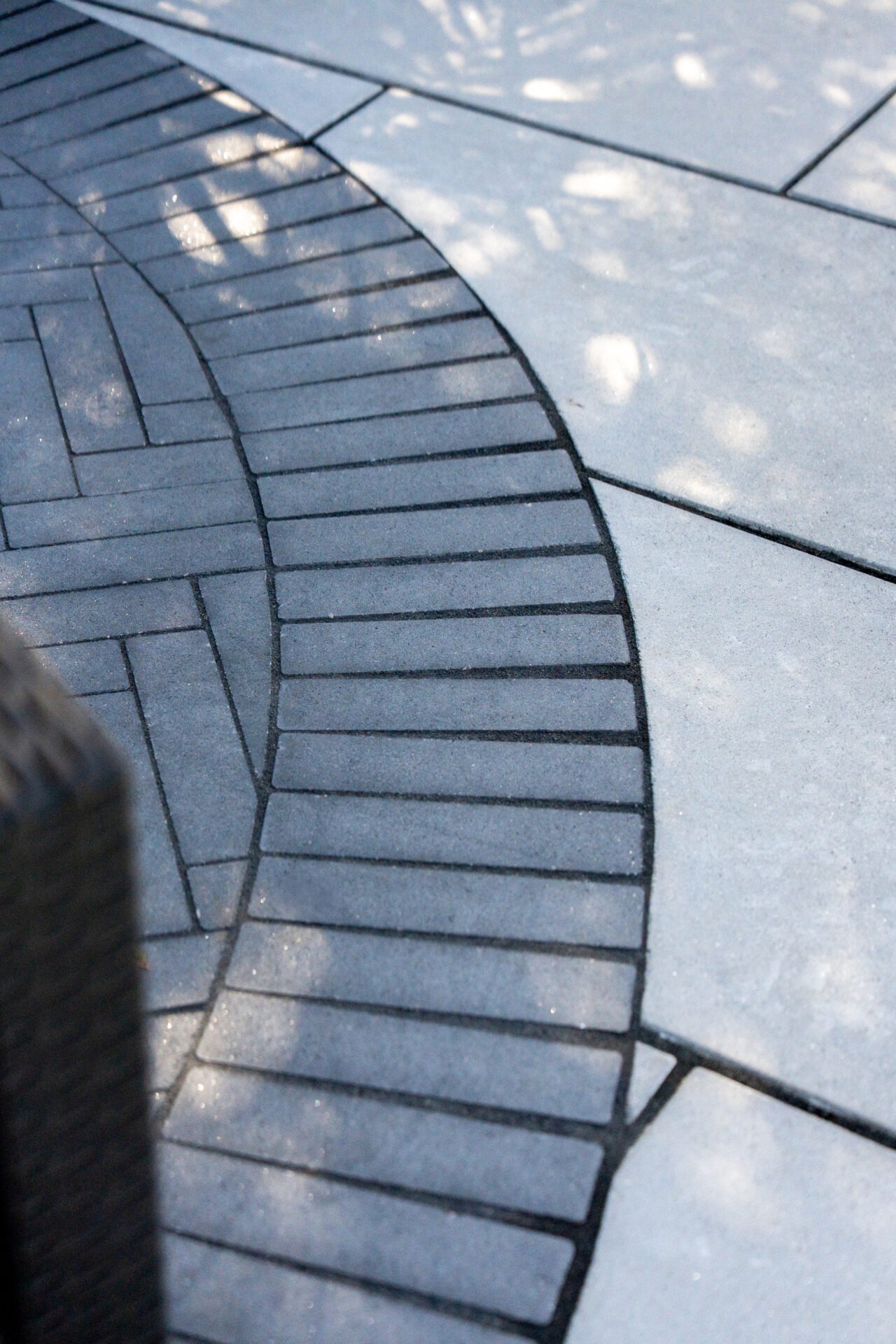 Close-up of curved dark grey pavers transitioning into a large light grey stone patio surface.