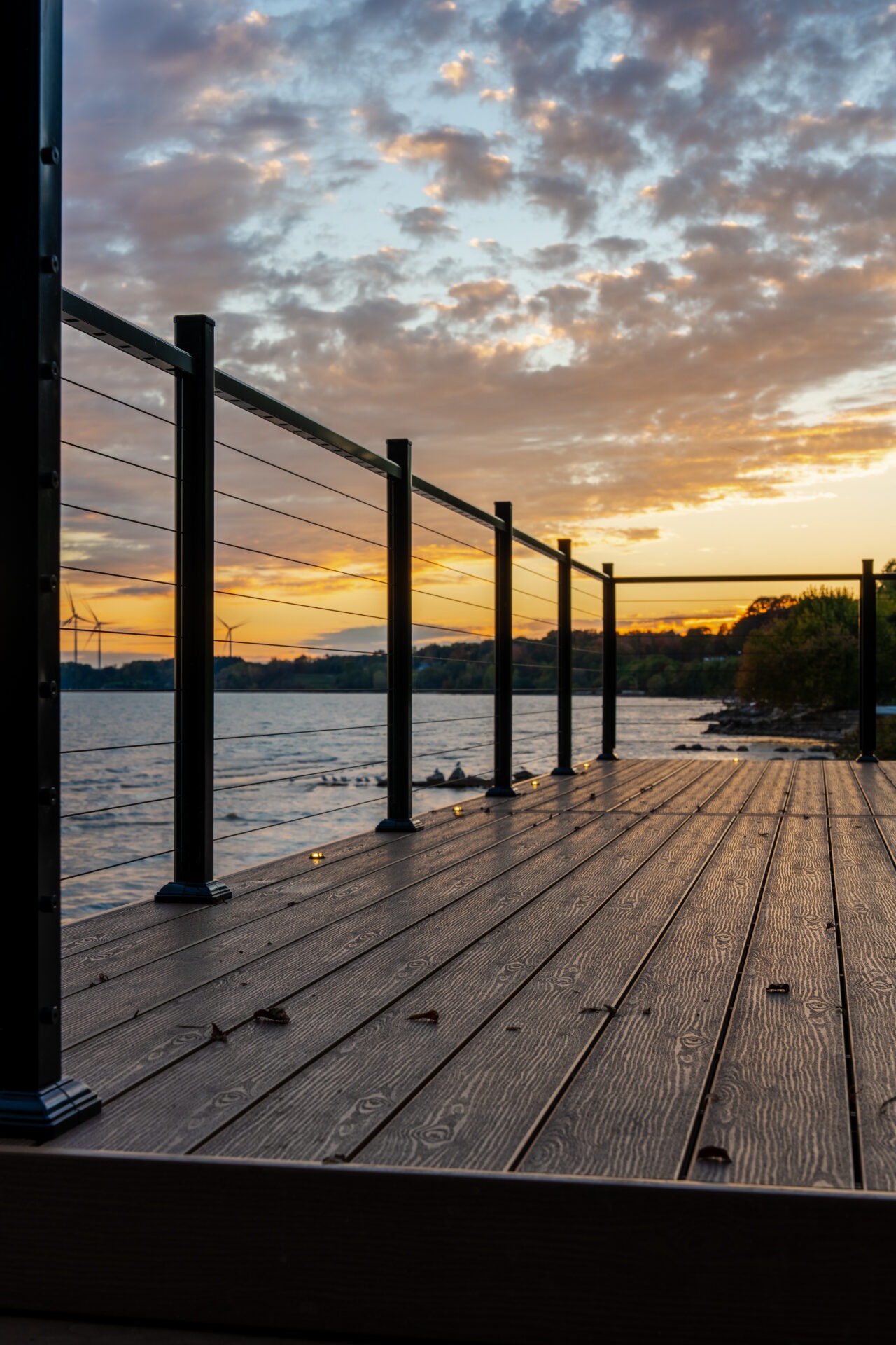 Perspective view along a modern deck with cable railings overlooking a vast lake at twilight.