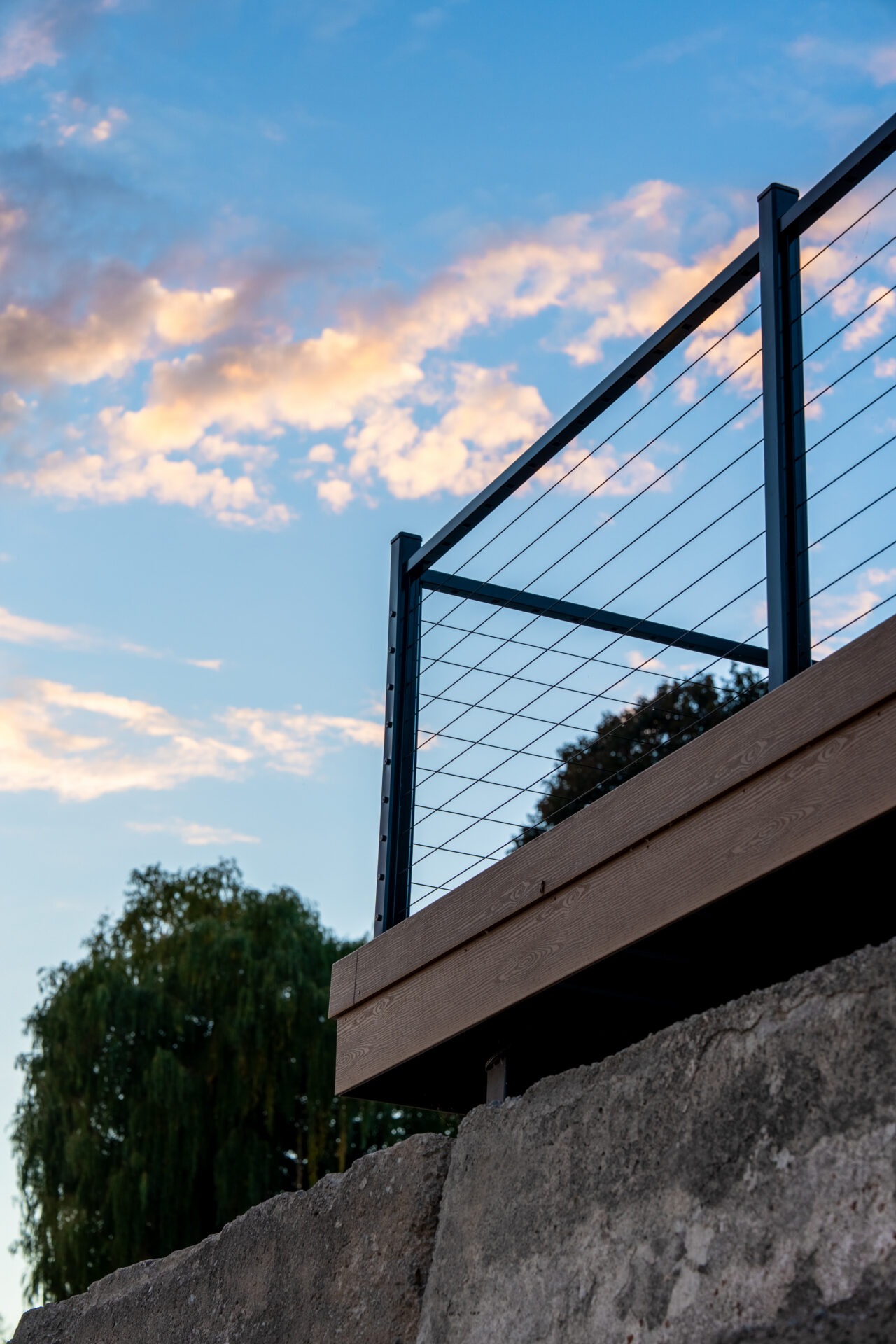 Low-angle shot of a deck corner with cable railings against a blue sky with soft, sunset clouds.