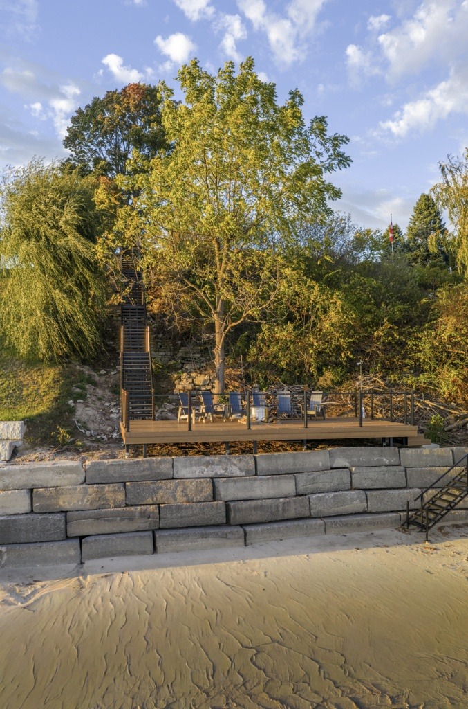 Shoreline deck with Adirondack chairs and a fire pit, featuring a long staircase rising up the sloped bank.