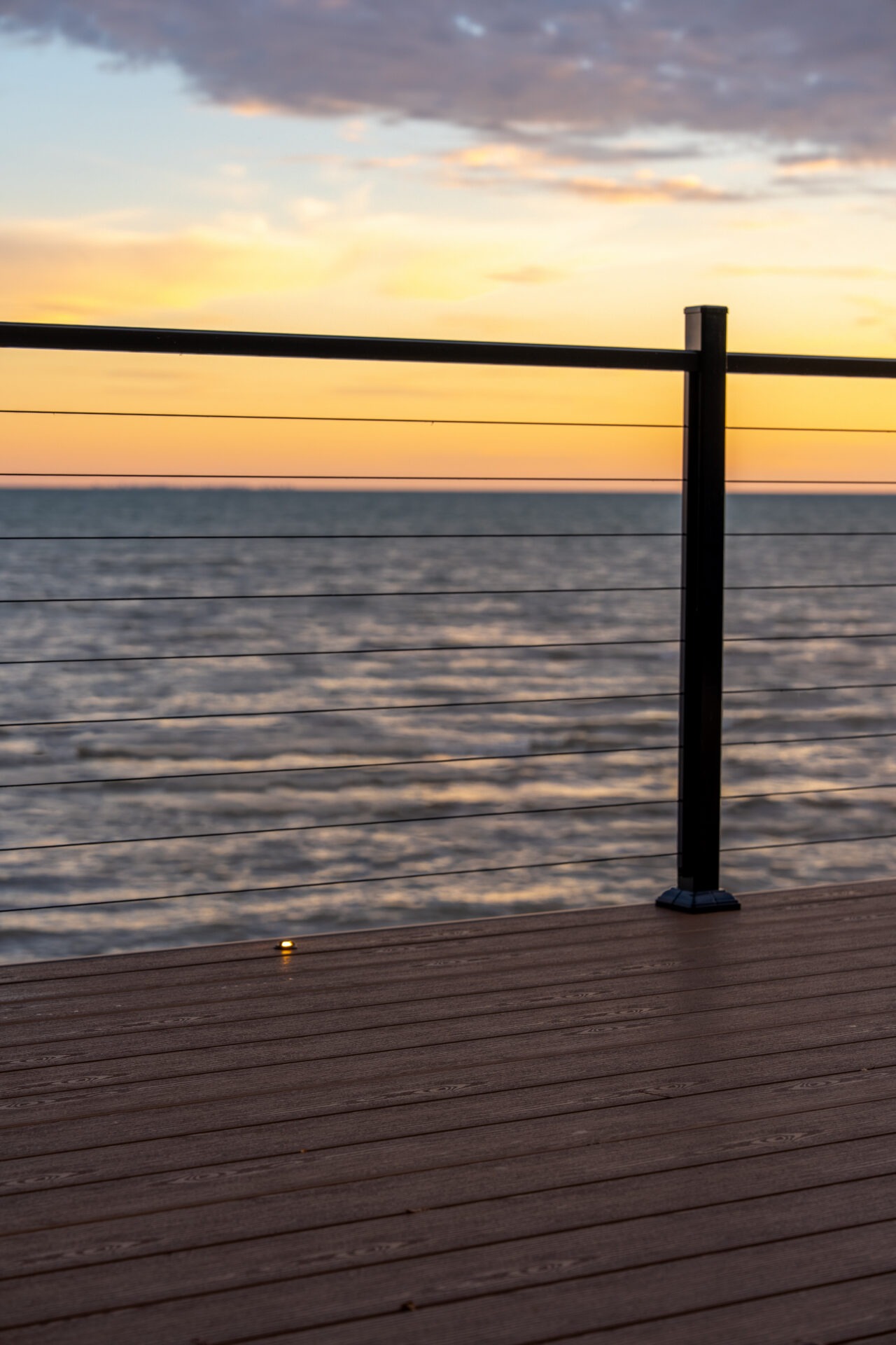 Silhouette of a deck railing against a vibrant orange and yellow sunset over the water.