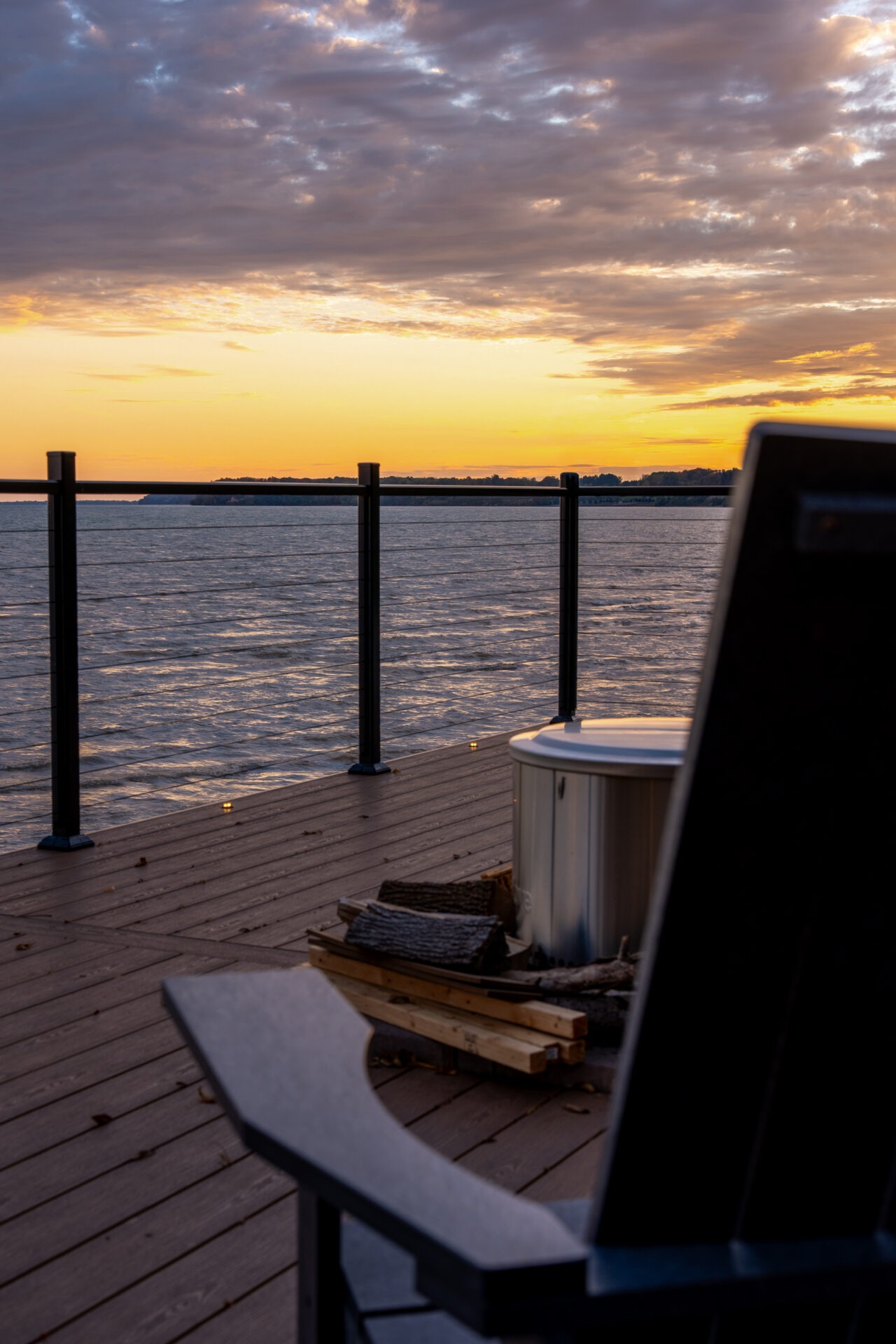 Close-up of a deck fire pit and the back of a chair with a sunset view over the lake in the background.