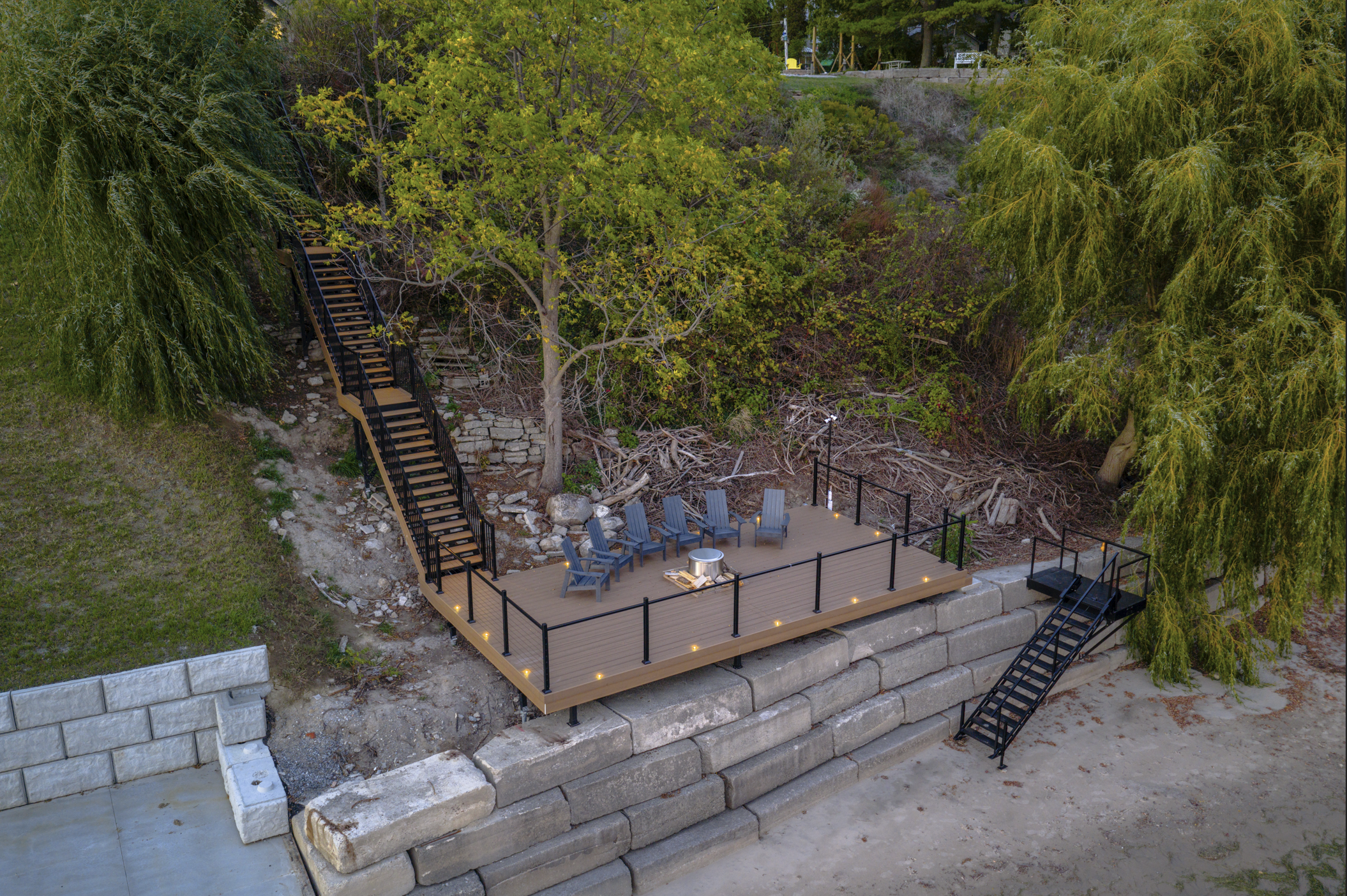 Wide aerial shot of a shoreline deck and long hillside staircase with integrated deck lighting at dusk.