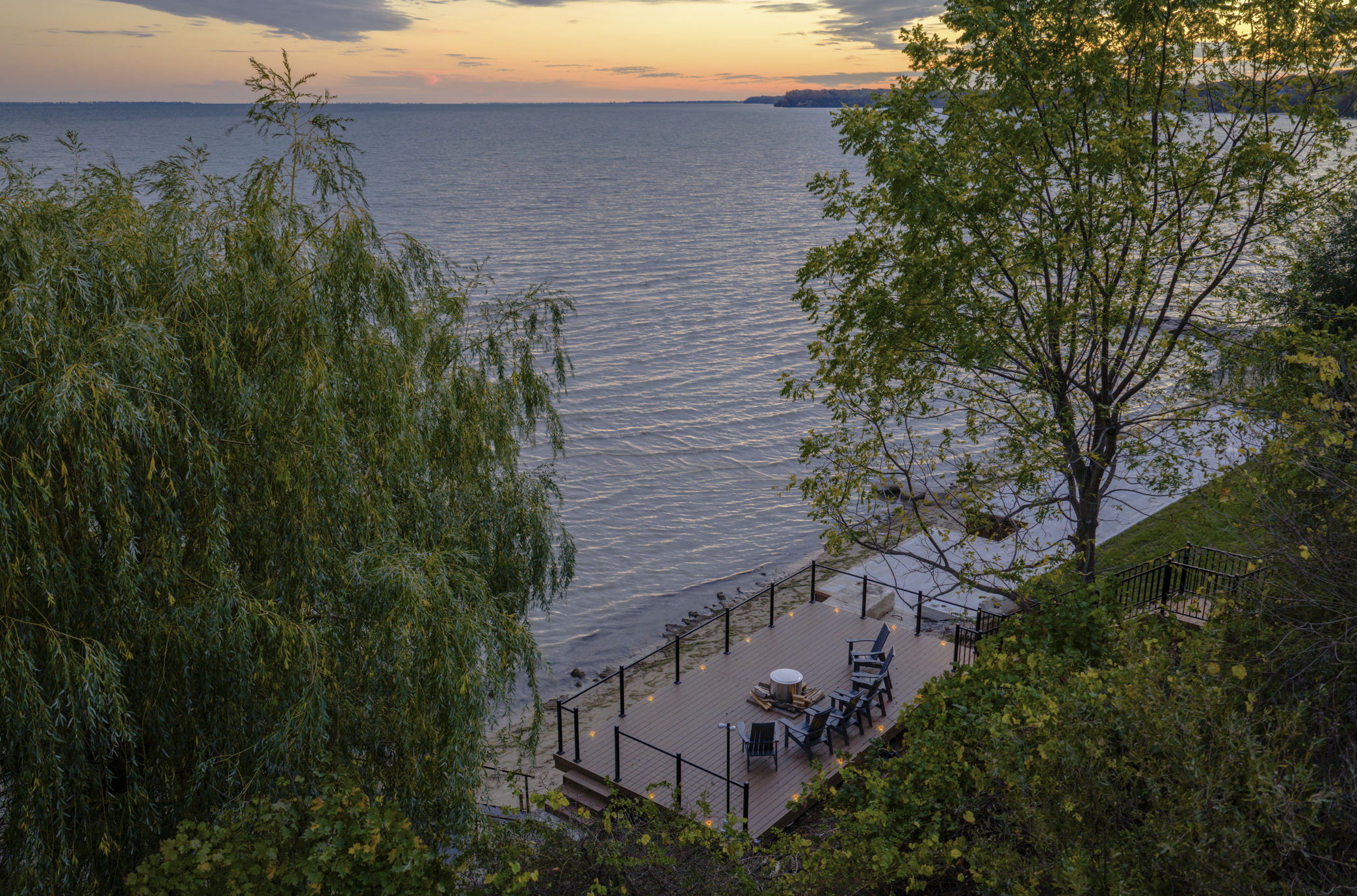 High-angle view of a shoreline deck at sunset, surrounded by lush trees and overlooking a calm lake.